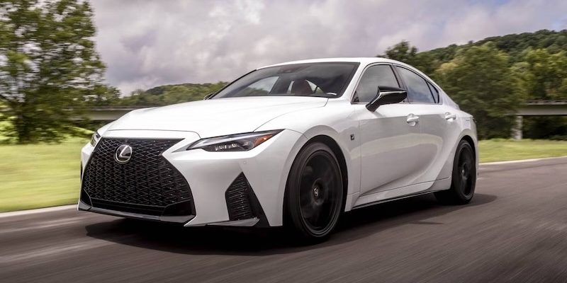 A white 2025 Lexus IS drives on a road.