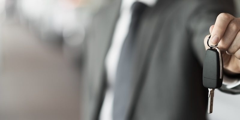 A dealership salesman hands over the keys to a used vehicle.